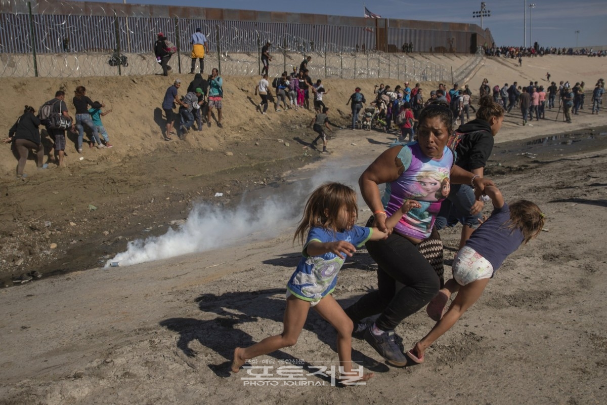 Maria Meza, a 40-year-old migrant woman from Honduras, part of a caravan of thousands from Central America trying to reach the United States, runs away from tear gas with her five-year-old twin daughters Saira Mejia Meza (L) and Cheili Mejia Meza (R) in front of the border wall between the U.S and Mexico, in Tijuana, Mexico on November 25, 2018. (Kim Kyung Hoon) [사진출처 : The Pulitzer Prizes 홈페이지]
